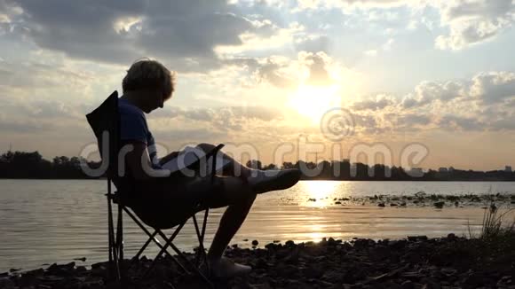 斯洛莫日落时分聪明人坐在河岸上读书写字视频的预览图