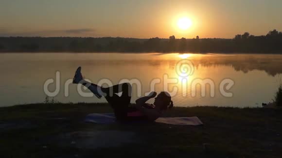 女孩在湖边日落时训练她的腹肌视频的预览图