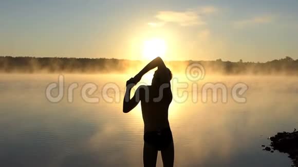 日落时分年轻人在湖岸伸展手臂视频的预览图