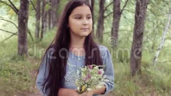 肖像一个小美丽的女孩正走在大自然上手里拿着一束花看着它慢慢视频的预览图