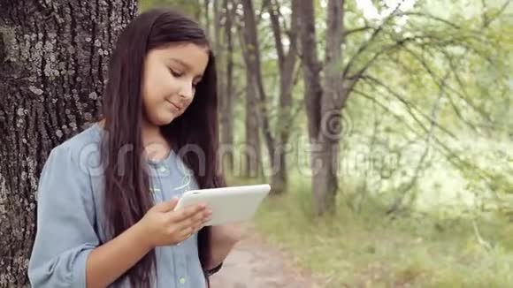 肖像一个漂亮的女孩站在树旁用平板电脑笑视频的预览图