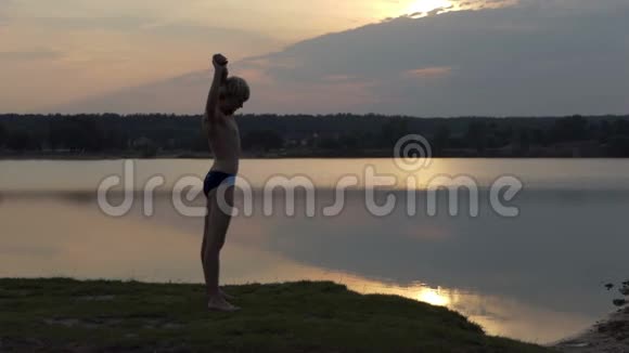 年轻人把肩膀伸到懒腰的湖岸上视频的预览图