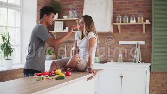 一对迷人的多民族夫妇清晨在厨房里聊天的慢镜头帅哥在喂他视频的预览图