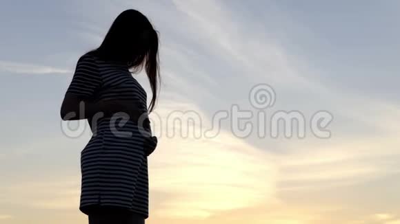 美丽的孕妇站在夕阳西下的湖岸上视频的预览图
