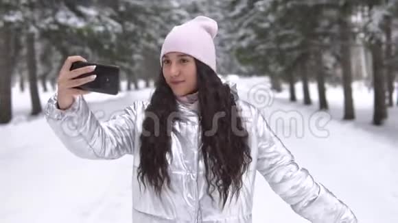 一个女孩在冬天的森林里用智能手机自拍视频的预览图