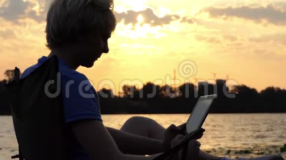 明亮的人坐在折叠椅上看着他的平板电脑在日落视频的预览图