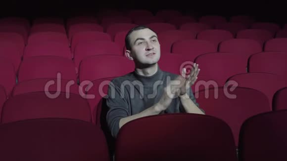 单身男子坐在黑暗电影院舒适的红色椅子上鼓掌视频的预览图