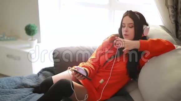 可爱的女孩在家沙发上用耳机听音乐视频的预览图