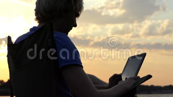 男人坐在折叠椅上看着他的平板电脑在日落在斯隆莫视频的预览图