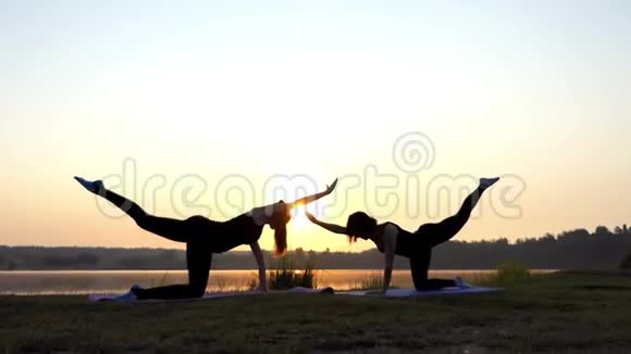 两个女孩站在日落湖畔的四人瑜伽垫上视频的预览图