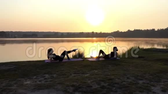两个苗条的女孩躺在垫子上每人抬起一只腿在日落时微笑视频的预览图