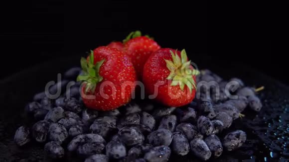 金银花和草莓的深色浆果在黑色背景下旋转视频的预览图