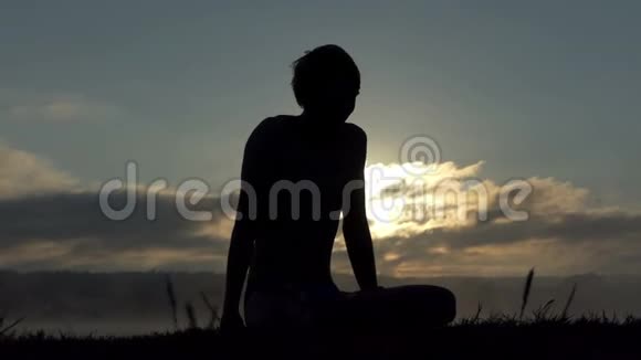 性感男人坐在湖畔在日落时慢动作练习瑜伽视频的预览图