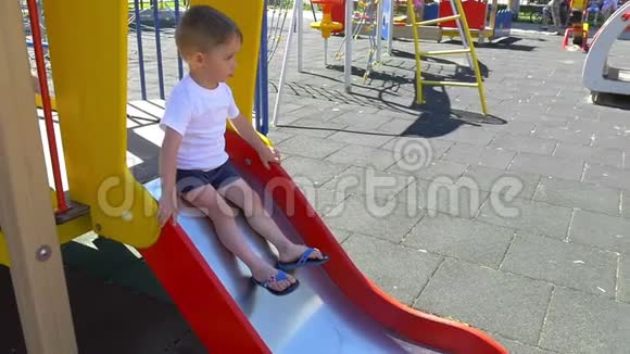 一个非常高兴的小男孩慢悠悠地在操场上玩滑梯视频的预览图