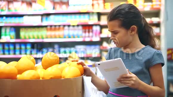 在杂货店买数字平板电脑的小女孩在网上买橘子水果超市里的小女孩视频的预览图