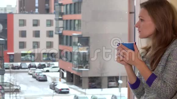 担心的女人坐在窗边喝杯咖啡茶雪花飘落视频的预览图