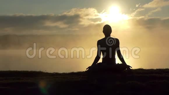 闪闪发光的男人坐在湖边在日落时慢动作练习瑜伽视频的预览图