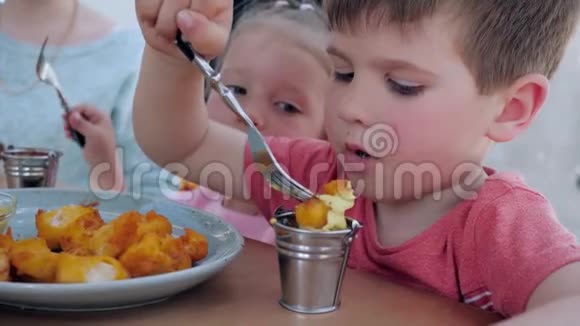 小双胞胎正在吃带有酱汁的炸鸡块男孩和女孩正在餐馆吃一顿开胃的晚餐视频的预览图