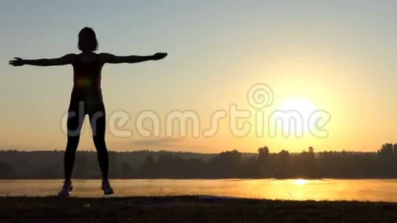 女人跳起来双手紧握在邋遢的夕阳下视频的预览图