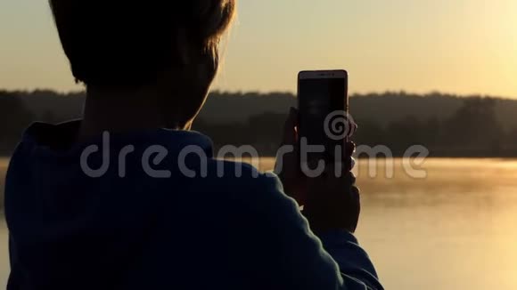 女人在4k的夏季日落时拍摄一个野湖视频的预览图