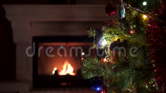 令人惊叹的圣诞树闪烁着五颜六色的灯光花环靠近壁炉燃烧着的火木视频的预览图
