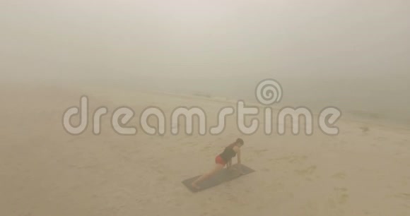 在多雾天气下美丽的女孩在沙滩上伸展双腿视频的预览图