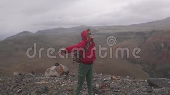 年轻女子在山上一个狂野美丽的地方旅游雨中的女孩在山口带着一个视频的预览图