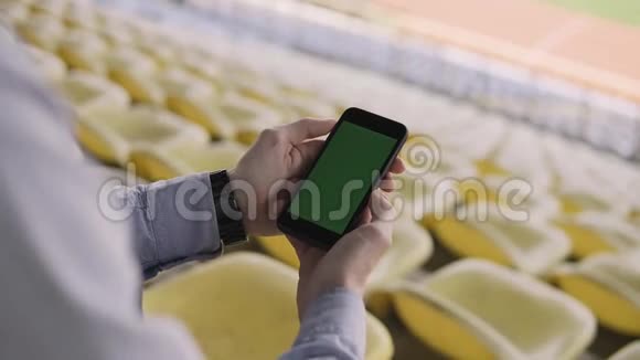 男子使用智能手机在体育场内看着手机上的绿色屏幕视频的预览图
