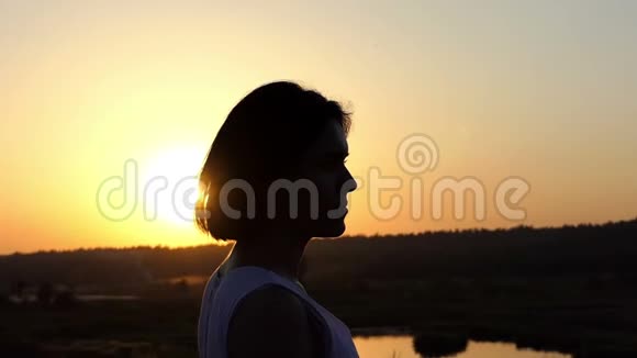 年轻的布鲁内特女士在日落的湖岸上令人印象深刻地转过头视频的预览图