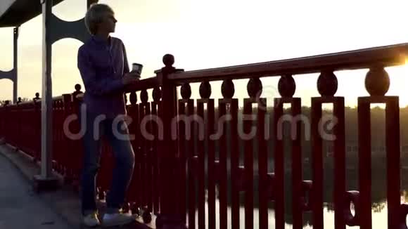 浪漫的男人从纸杯中喝咖啡在桥上享受日落视频的预览图