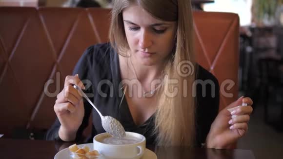 年轻漂亮的女人坐在咖啡馆里开胃地吃着热奶油汤视频的预览图