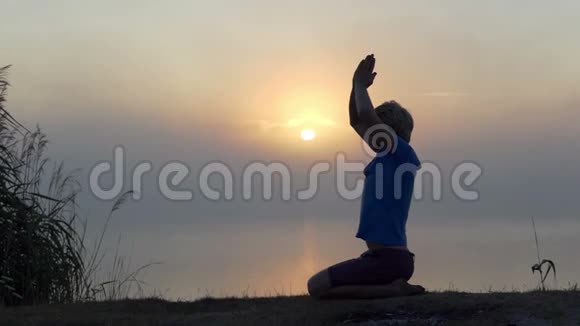 夕阳西下年轻人坐在湖岸上祈祷视频的预览图