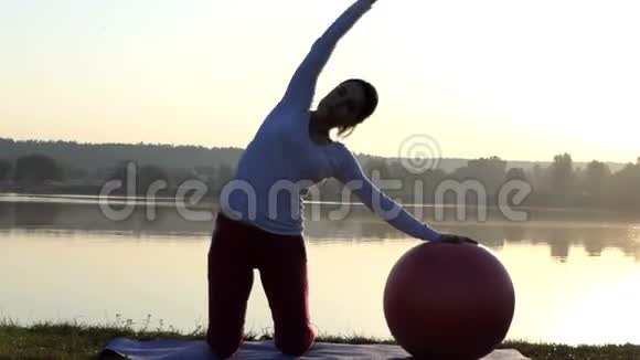苗条的女人在日落时跪在一个健身球旁边视频的预览图