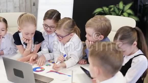 穿西装的孩子们在办公室的桌子上看着图表和说话视频的预览图