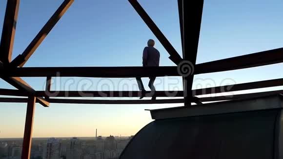 金发碧眼的男人坐在太阳落山的金属建筑上视频的预览图