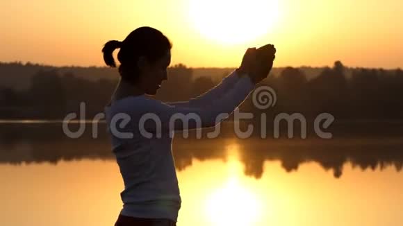 一个苗条的女人在日落时旋转她的手臂和弯曲视频的预览图