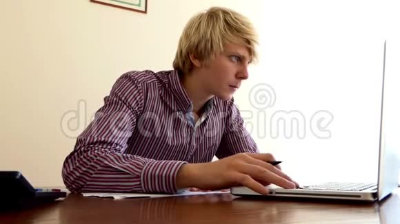 年轻人在办公室里写了一份文件看着他的计算器和一台电脑视频的预览图