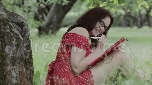 小女孩坐在树下的草地上写笔记视频的预览图