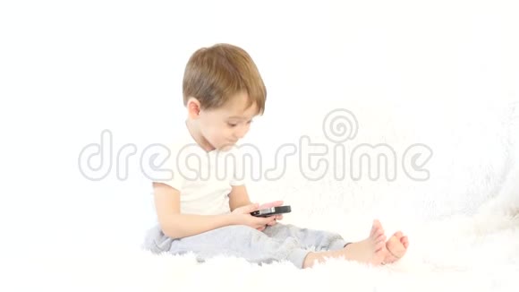 快乐的孩子在白色背景下玩智能手机一个孩子坐在白色沙发上视频的预览图