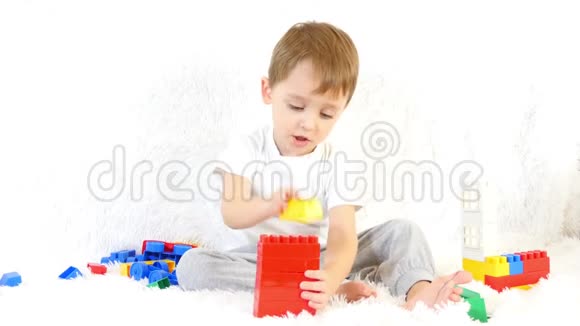 快乐的孩子坐在沙发上玩彩色积木坐在白色背景上视频的预览图
