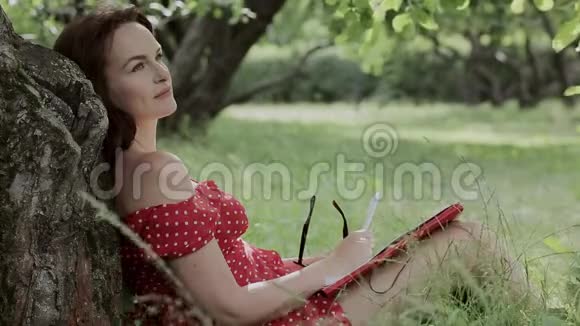 小女孩坐在树下的草地上写笔记视频的预览图
