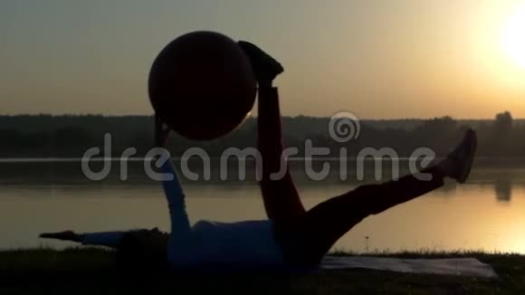 一个懒散的女人躺在垫子上日落时手里拿着一个健身球视频的预览图