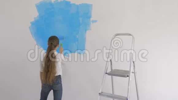 年轻女孩在房间里用蓝色油漆用滚筒油漆墙纸视频的预览图