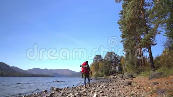那个带着红色背包的旅行者的女人去了山湖的海岸海滩上有一个黄色的帐篷视频的预览图