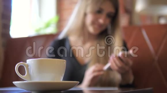 把注意力集中在杯子上一个女人在后台使用智能手机是模糊的视频的预览图