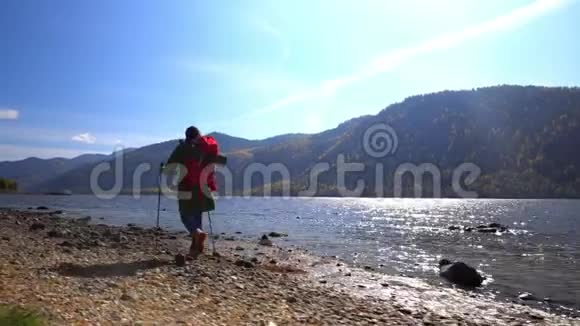 那个带着红色背包的旅行者的女人去了山湖的海岸海滩上有一个黄色的帐篷视频的预览图