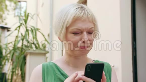 年轻的金发女人坐在外面用电话视频的预览图