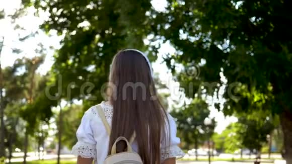 背着背包的女孩戴着耳机去公园听音乐微笑着十几岁的孩子高兴地挥手视频的预览图