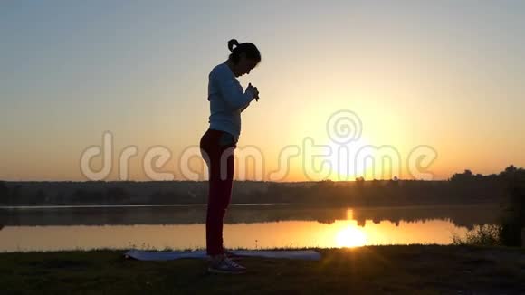 夕阳西下一个苗条的女人在她的垫子上弯腰驼背视频的预览图