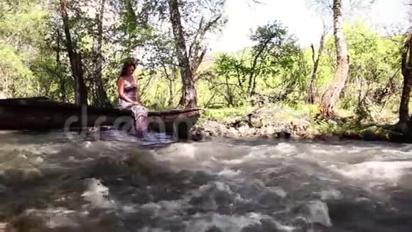 一个漂亮的女孩坐在桥上玩她的腿桥下有一条河视频的预览图